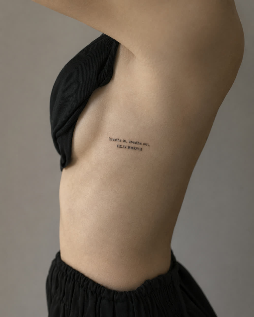 Small lettering and numeral tattoo along the ribs